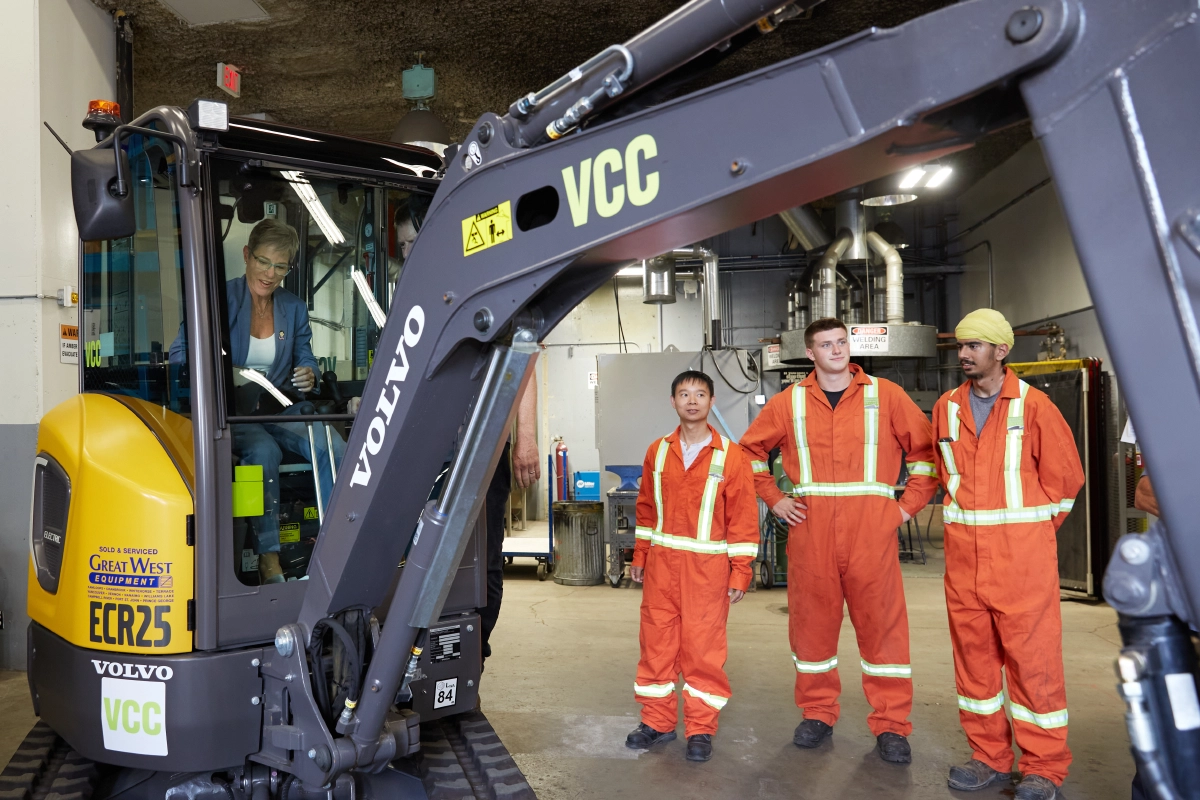 Candid photograph of Corporate media event with BC cabinet minister and students operating heavy machinery