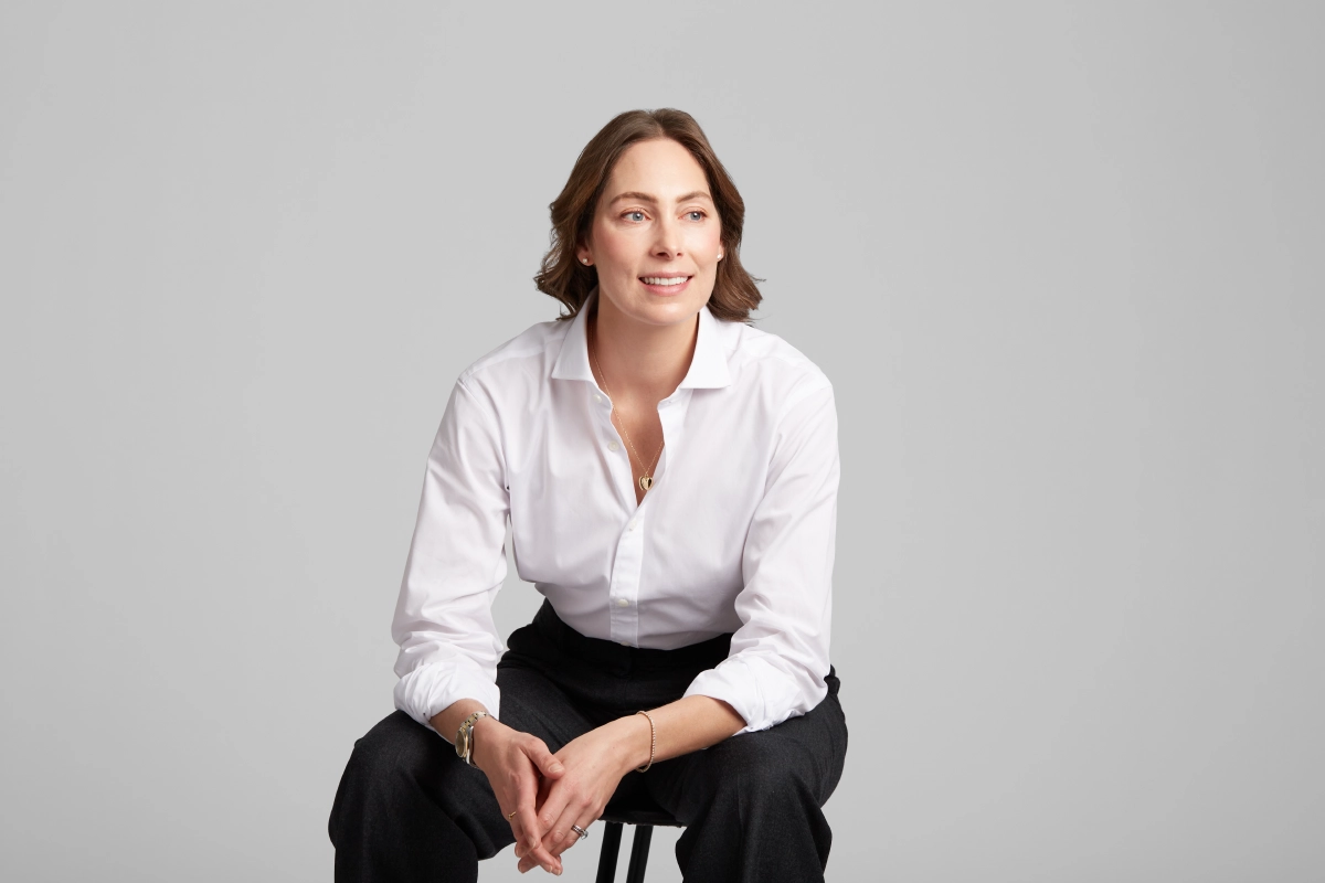 professional corporate headshot of female executive in dark pants and white shirt seated and looking away on a light grey background taken in a Vancouver office