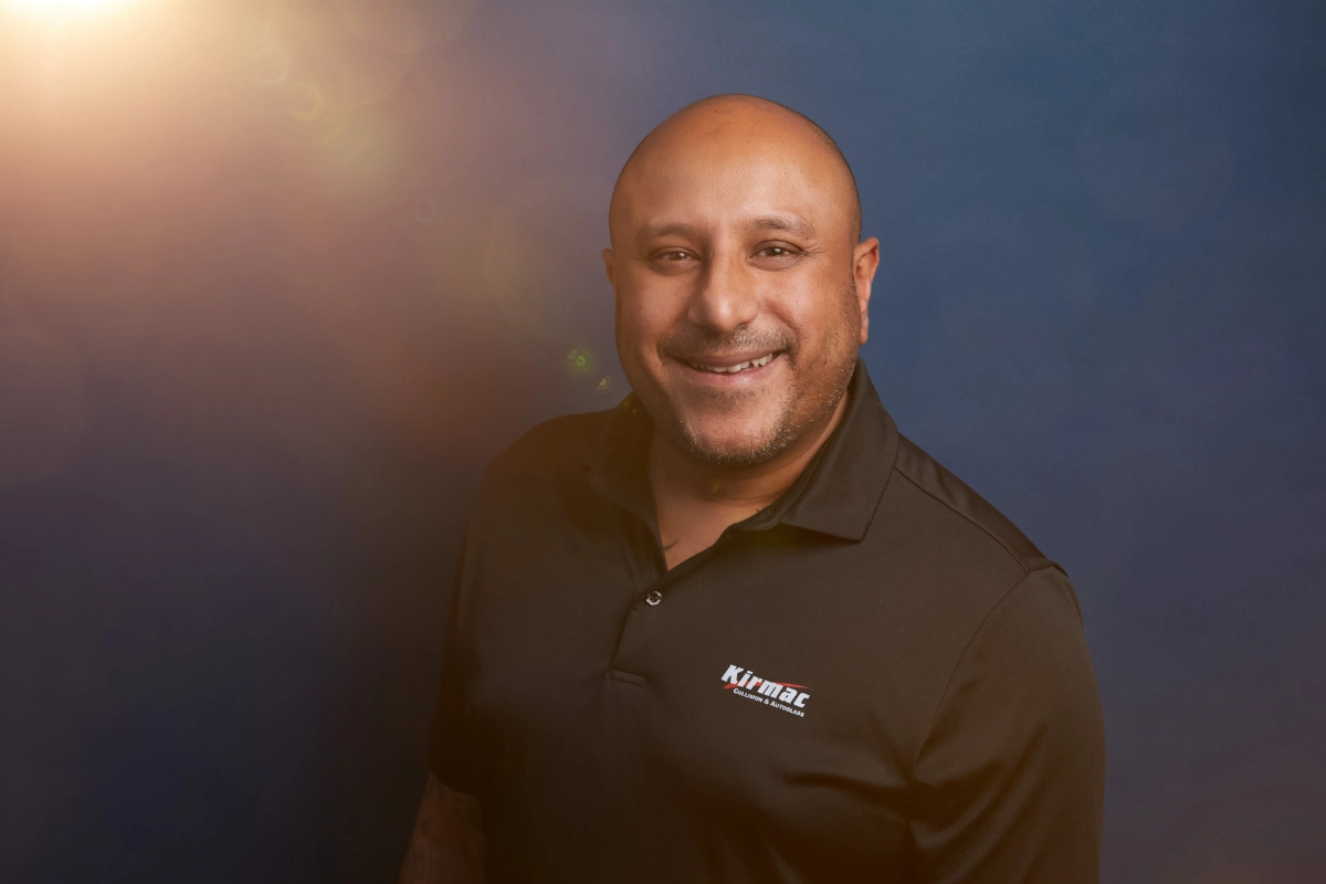 Corporate headshot of male executive in branded shirt on a blue background with flared lighting