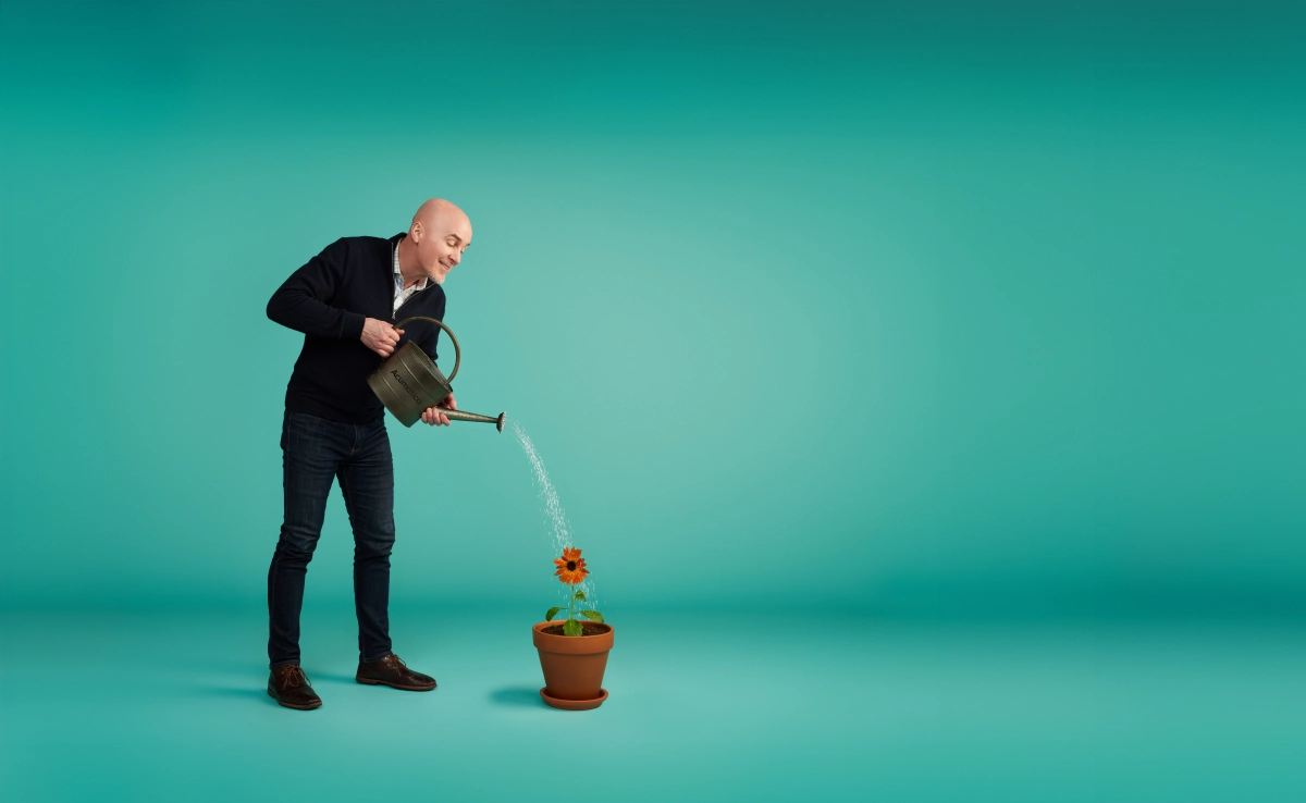 male in black clothes watering a flower pot on a light blue background taken in a Vancouver photography studio